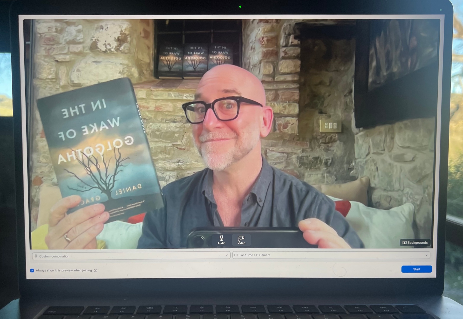 Daniel Grace on a virtual interview from Tuscany holding In the Wake of Golgotha